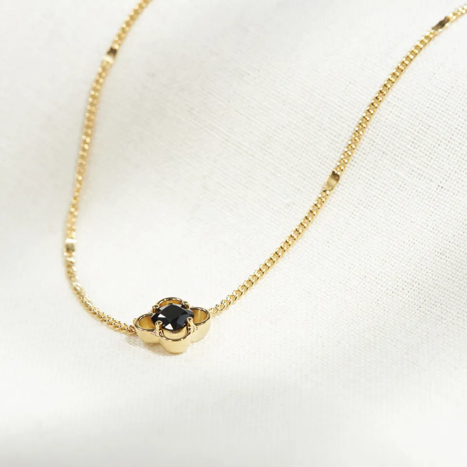 Natural black onyx set in an 18K gold vermeil Petite Quatrefoil pendant, resting on cream linen