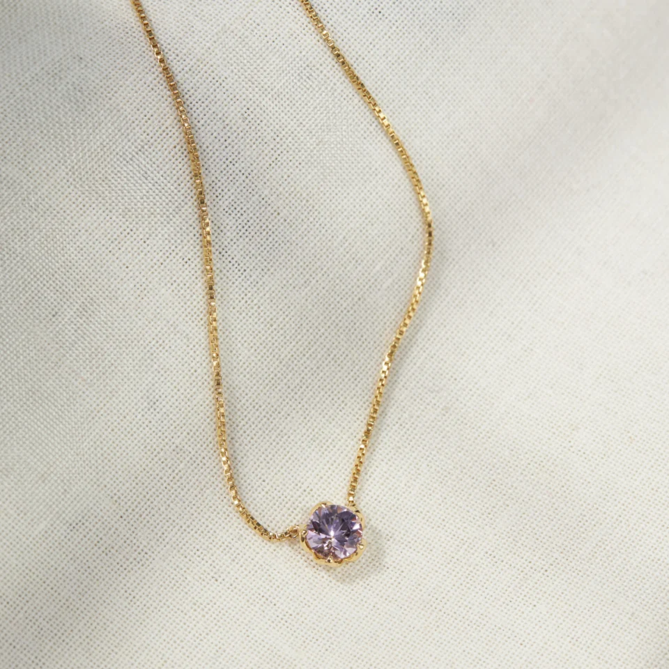 Natural lavender amethyst set in an 18K gold vermeil Sparkle Borage pendant, resting on cream linen