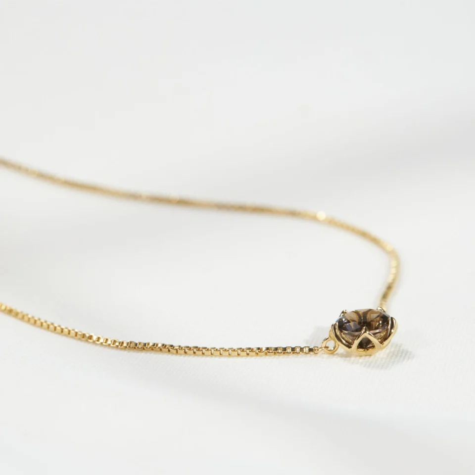 Natural smoky quartz set in an 18K gold vermeil Sparkle Borage pendant, resting on cream linen