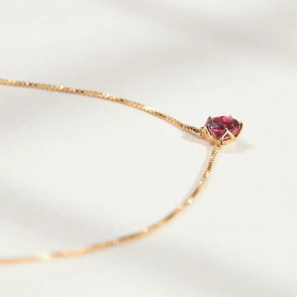 Natural rhodolite garnet set in an 18K gold vermeil Sparkle Borage pendant, resting on cream linen