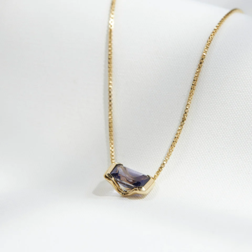 Natural iolite set in an 18K gold vermeil Octagonal pendant, resting on cream linen