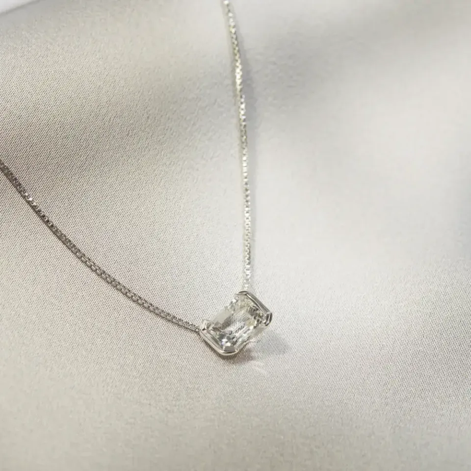 Natural white topaz gemstone in an emerald cut sterling silver pendant, resting on white satin